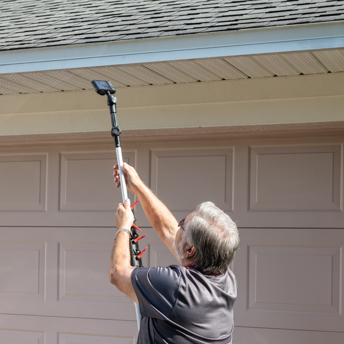 Home inspector using a pole camera to inspect the roof edge and soffit of a house